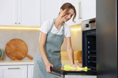 Kadın mutfakta mikrofiber bezle fırını temizliyor.