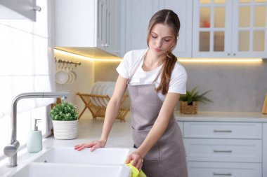 Mutfak lavabosunu evde mikrofiber bezle silen bir kadın.