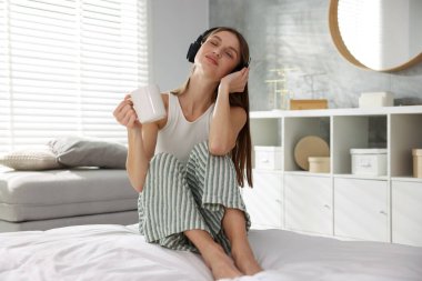 Kahveli güzel bir kadın evde yatağında müzik dinliyor.