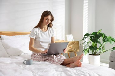 Elinde kahve olan bir kadın evde dizüstü bilgisayarla çalışıyor.