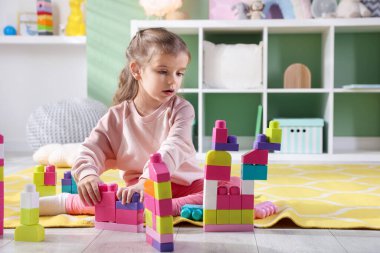 Küçük kız oyun odasında yerde oyuncaklarla oynuyor.