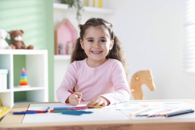 Masada pastel boyayla resim çizen sevimli küçük kız.