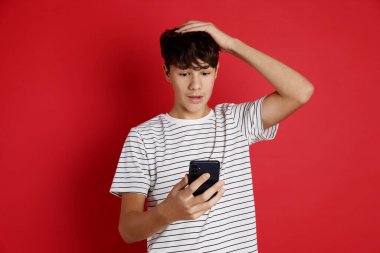 Kırmızı arka planda akıllı telefonu olan genç bir çocuk.