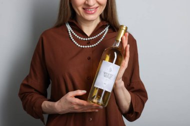 Açık gri arka planda beyaz şarap şişesi olan profesyonel şarap garsonu, yakın plan.