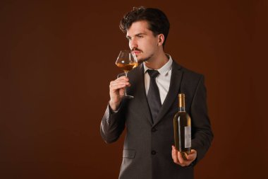 Profesyonel şarap garsonu kahverengi arka planda beyaz şarap tadıyor.