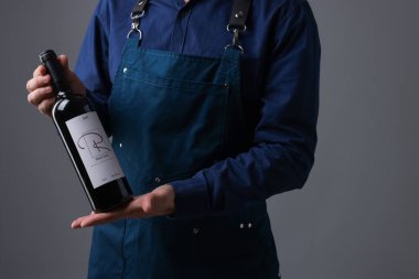 Gri arka planda kırmızı şarap şişesi olan profesyonel şarap garsonu.