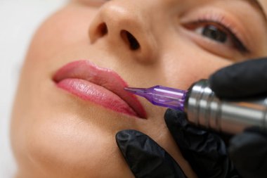 Güzellik uzmanı genç bayana kalıcı dudak makyajı yapıyor.