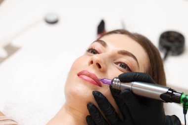 Güzellik uzmanı içeride genç bir kadına kalıcı dudak makyajı yapıyor, yakın plan. Metin için boşluk