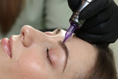 Güzellik uzmanı genç bayana kalıcı kaş makyajı yapıyor.