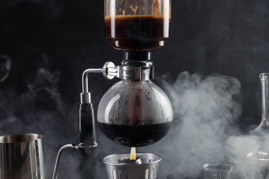 Vakumlu kahve makinesinde aromatik kahve demlemek siyah arka planda, dumanlı, yakın plan.