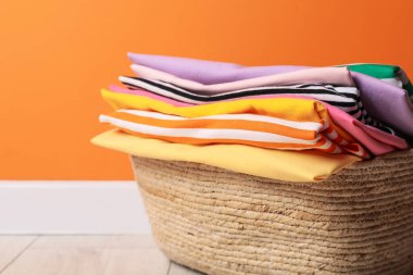 Çamaşır sepetinde yerde, turuncu duvarın yanında giysiler var. Kapalı. Metin için boşluk