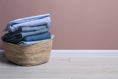 Çamaşır sepetinin içinde bej duvarın yanında giysiler var. Metin için boşluk