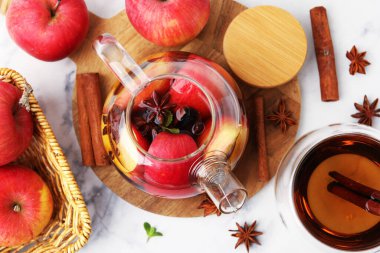 Aromatik meyve çayı cam çaydanlıkta, fincan, elma ve baharatlar beyaz mermer masada, düz yerde.