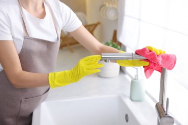 Evinde mikrofiber bezle mutfak musluğunu temizleyen kadın, yakın çekim.