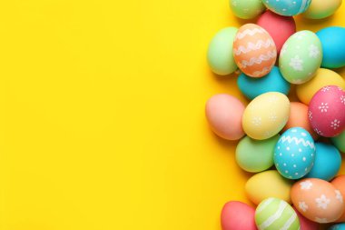 Many painted Easter eggs on yellow background, flat lay. Space for text