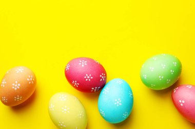 Many painted Easter eggs on yellow background, flat lay. Space for text