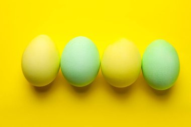 Many painted Easter eggs on yellow background, flat lay