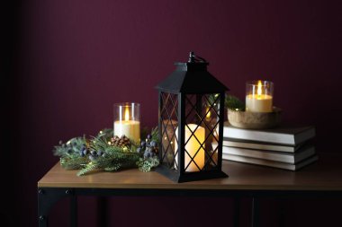 Noel feneri, yanan mumlar, kitaplar ve dekoru koyu pembe arka plana karşı ahşap masada.