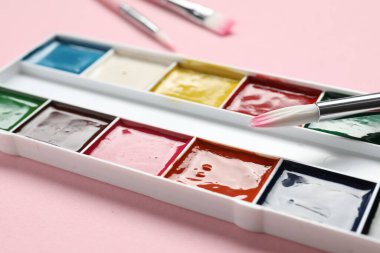 Pembe arka planda suluboya boya ve fırçalı palet, yakın plan.