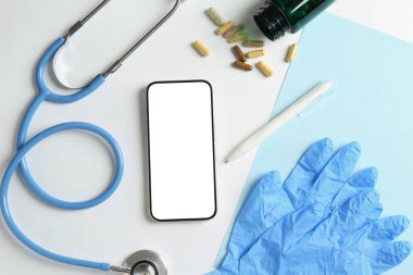 Sağlığınıza. Akıllı telefon, steteskop, tıbbi eldivenler, haplar ve arka planda kalem, düz konum