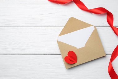 Envelope with love letter, red heart and ribbon on white wooden table, flat lay. Space for text