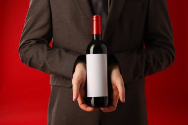 Kırmızı arka planda şarap şişesi olan profesyonel şarap garsonu, yakın plan.