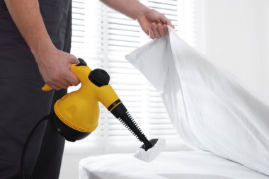 Haşere kontrol işçisi yatağı temizliyor, kapalı alanda buhar temizleyicisiyle, yakın plan