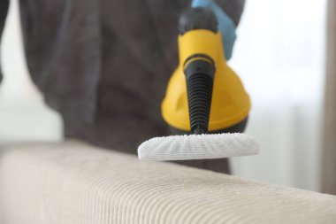 Haşere kontrol işçisi kanepeyi temizliyor. Kapalı alanda buhar temizleyicisi var.