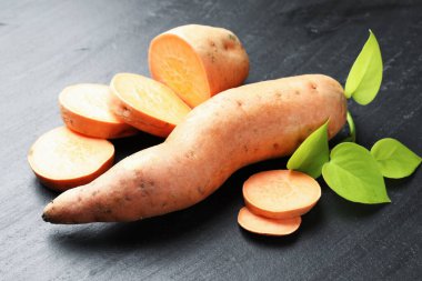 Tüm, tatlı patatesler ve yeşil yapraklı dallar koyu dokulu masa, yakın çekim