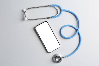 Sağlığınıza. Işık arka planında akıllı telefon ve steteskop, düz konum