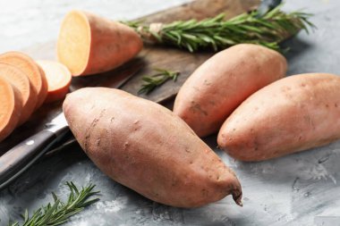 Çiğ patates, biberiye, ahşap tahta ve bıçak dokulu gri masada, yakın plan.