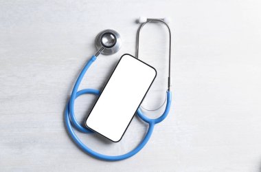 Sağlığınıza. Işık desenli masa üzerinde akıllı telefon ve steteskop, üst görünüm