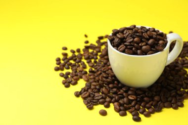 Aromatik kahve çekirdekleri ve fincanlar sarı arka planda, yakın plan. Metin için boşluk