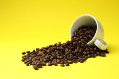 Aromatik kahve çekirdekleri ve ters çevrilmiş fincanlar sarı arka planda, yakın plan.