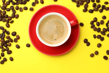 Sarı zemin üzerinde aromatik kahve ve fasulye olan bir fincan, düz uzanmış.