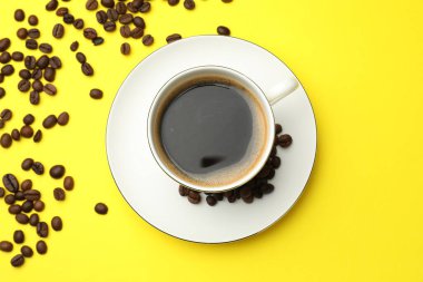 Kahveyi fincanda tazelemek ve sarı arka planda fasulye, düz uzanmak.