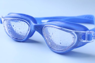 Açık mavi arkaplanda su damlaları olan yüzme gözlükleri, yakın plan