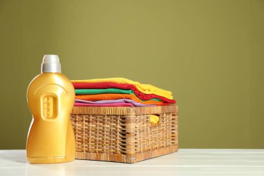 Çamaşır sepetinin içinde çamaşır ve deterjan beyaz ahşap masa üzerinde zeytin arka planına karşı, metin için boşluk