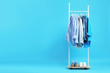 Askıda asılı farklı elbiseler ve açık mavi arka planda ayakkabılar, metin için boşluk