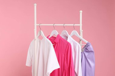 Farklı giysiler pembe arka planda asılı, yakın plan.
