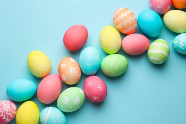Many painted Easter eggs on light blue background, flat lay