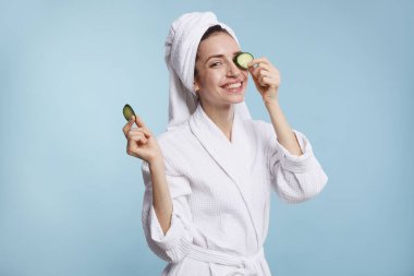Havluya sarılı güzel bir kadın ve açık mavi arka planda salatalık dilimleri.