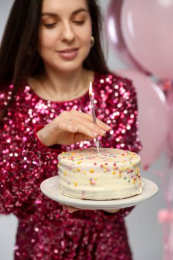 Doğum günü kutlaması. Kekin içine yanan mum ve balonlar koyan kadın açık gri arka planda, seçici odak