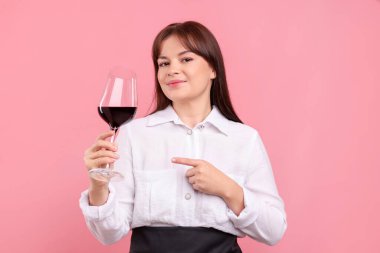 Profesyonel şarap garsonu, pembe arka planda bir bardak kırmızı şarap.