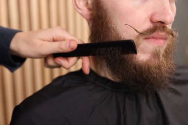 Berber berber dükkanında adamın sakalını tarıyor, yakın plan.