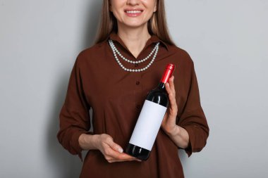 Açık gri arka planda şarap şişesi olan profesyonel şarap garsonu, yakın plan.