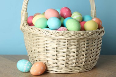 Güzel dekore edilmiş Paskalya yumurtaları hasır sepetin içinde ahşap masanın üzerinde açık mavi arka planda, yakın plan