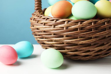 Güzel dekore edilmiş Paskalya yumurtaları hasır sepetin içinde beyaz ahşap masanın üzerinde açık mavi arka planda, yakın plan