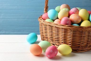 Güzel dekore edilmiş paskalya yumurtaları hasır sepetin içinde beyaz ahşap masanın üzerinde, yakın plan. Metin için boşluk