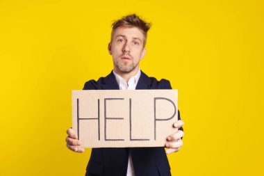 Mutsuz işadamı, elinde kelime yazılı karton tabela tutuyor. Sarı arka planda yardım.